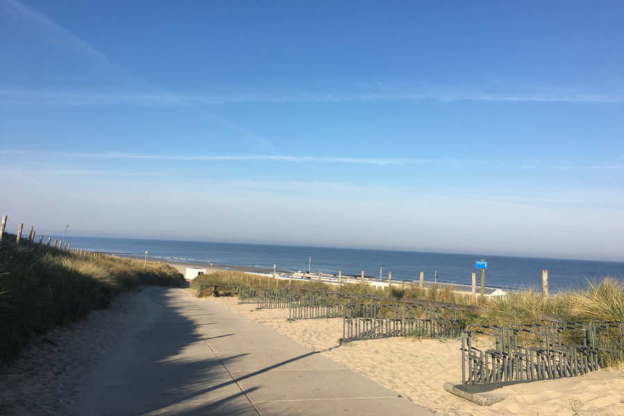 Foto Dünenweg zum Strand mit Fahrradständern rechts im Weg und am Horizont die Nordsee, darüber blauer Himmel
