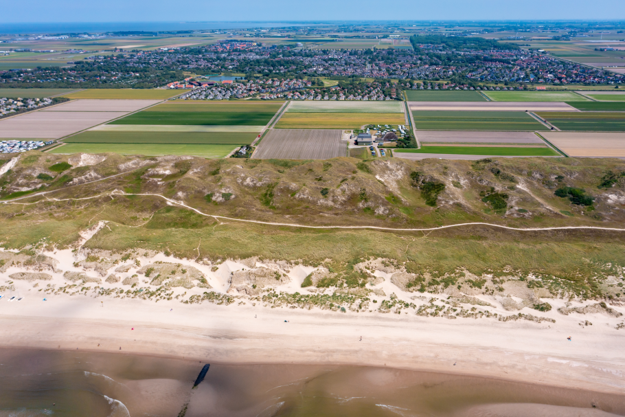 Foto Luftaufnahme vorne Meer, Strand und Dünen, in der Mitte Tulpenfelder und Wiesen, hinten die Häuser von Julianadorp