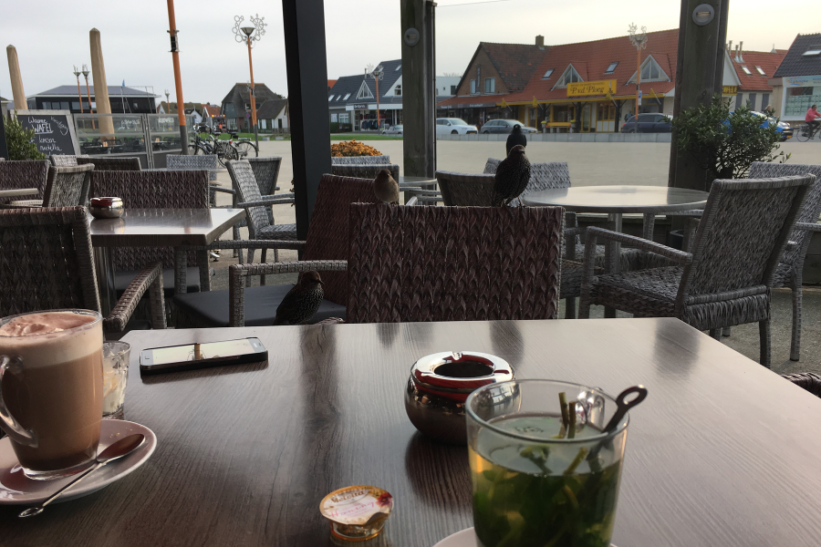 Foto Tisch im Cafe mit Teetasse und Kaffeetasse sowie Aussicht durchs Fenster auf den Dorfplatz