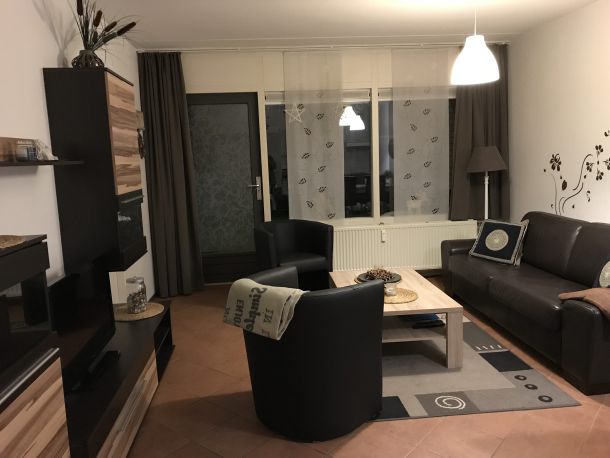 Foto Wohnzimmer mit Sofa, Sesseln, Tisch und Blick auf die Terassentür und die Fenster